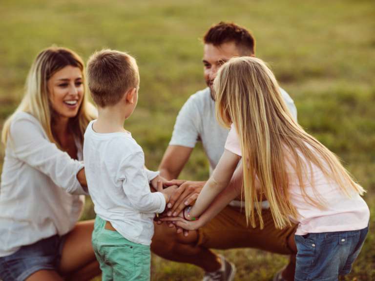 Junge Familie mit zwei Kindern kniet auf dem Boden und legt die Hände aufeinander