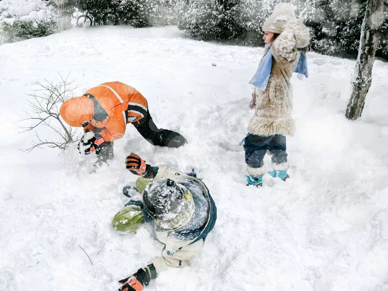 Drei Kinder spielen im Schneeanzug im Schnee