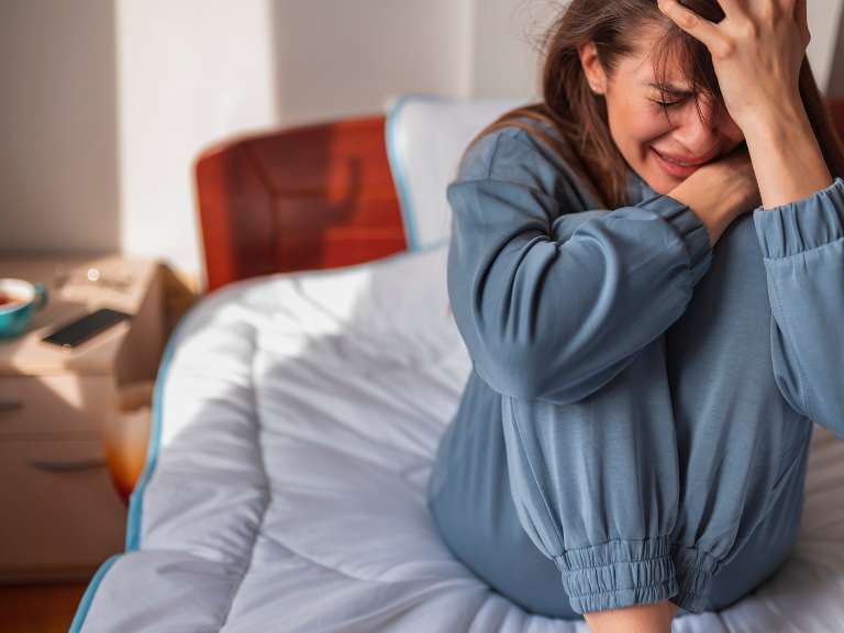 Frau hat Liebeskummer und sitzt weinend auf dem Bett