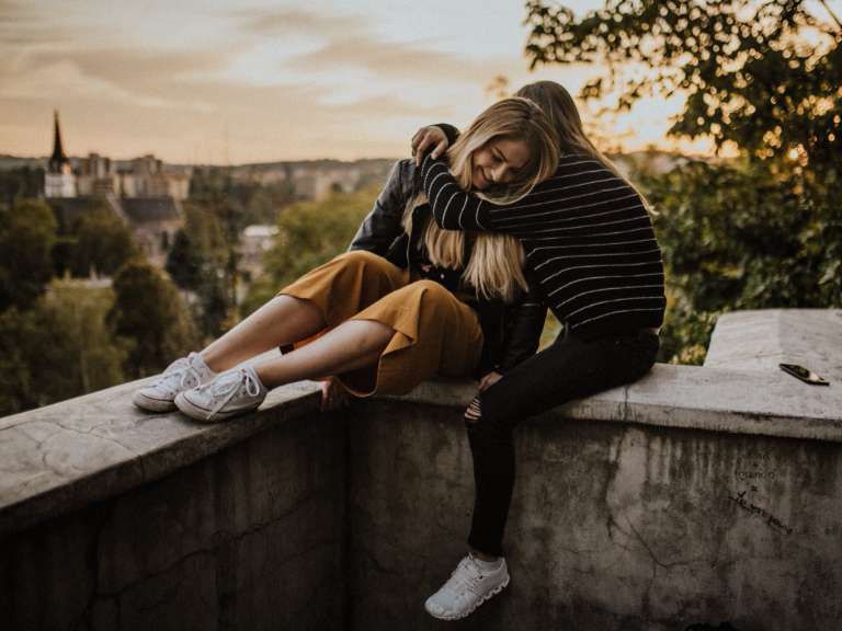 Zwei junge Frauen sitzen auf einer Mauer und umarmen sich