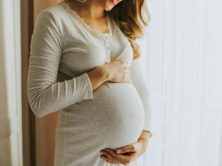 Werdende Mutter schaut auf ihren Babybauch und legt ihre Hände zart auf den Bauch