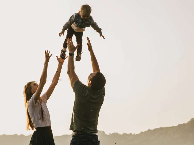 Junge Eltern sind mit ihrem Sohn in der Natur und werden ihn in die Luft und fangen ihn wieder auf