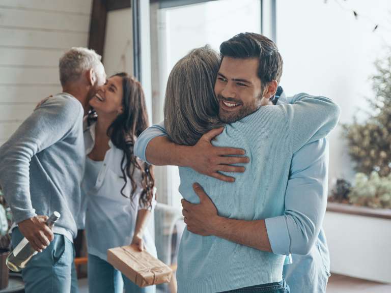 Junges Paar umarmt und begrüßt die Eltern des Mannes