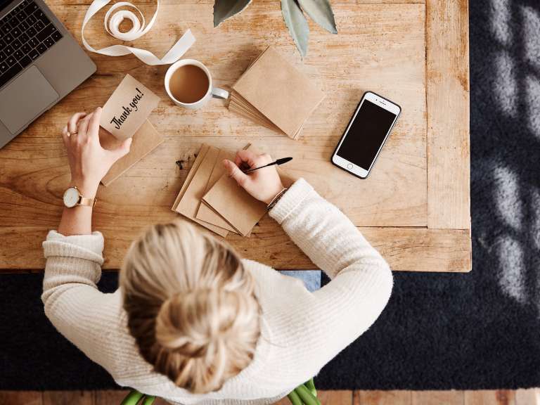 Frau sitzt am Schreibtisch und schreibt selbst Karten