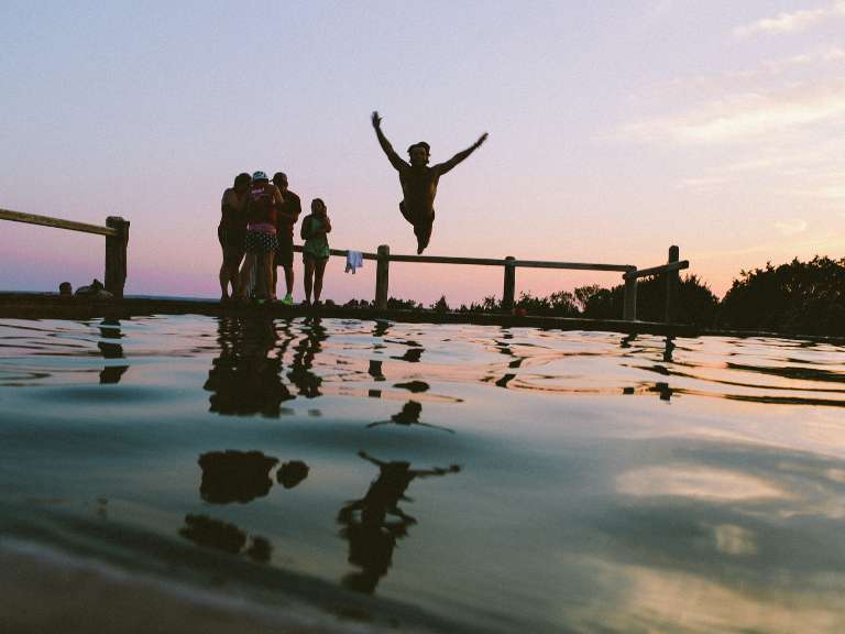 Gruppe von Teenagern ist am See bei Sonnenuntergang und springen ins Wasser