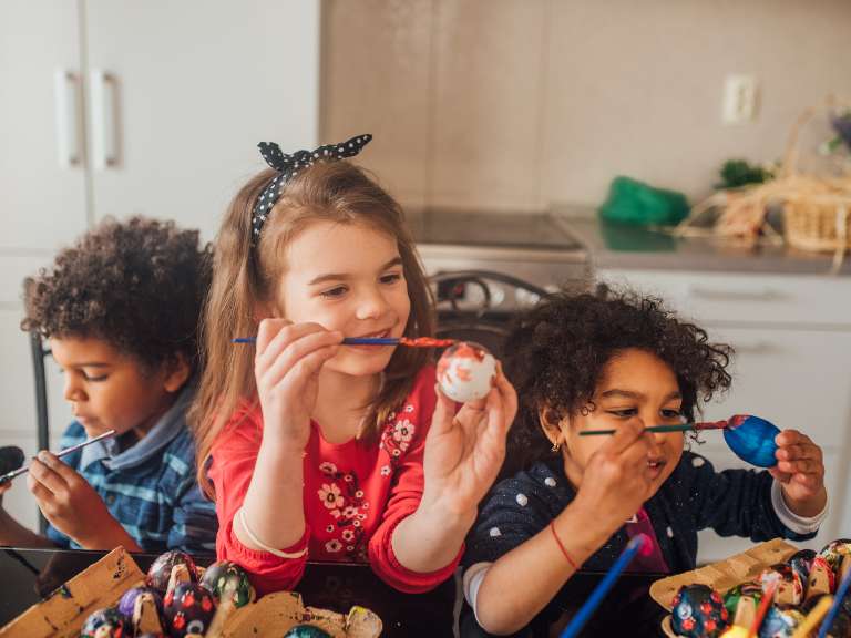 Drei Kinder bemalen mit einem Pinsel Eier zum Osterfest