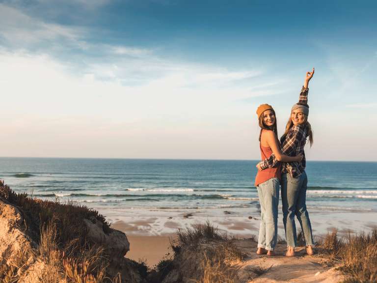 Zwei Freundinnen stehen am Strand und sehen glücklich aus