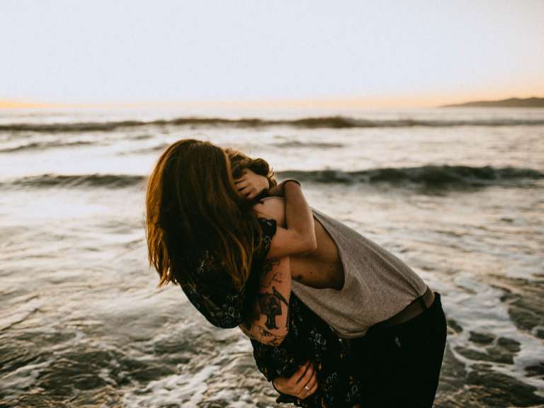 Junges Paar ist am Meer und umarmt sich, während es im Wasser steht