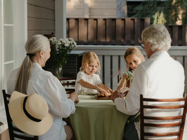 Zwei Kleinkinder sitzen mit ihren Großeltern an einem Tisch und spielen gemeinsam