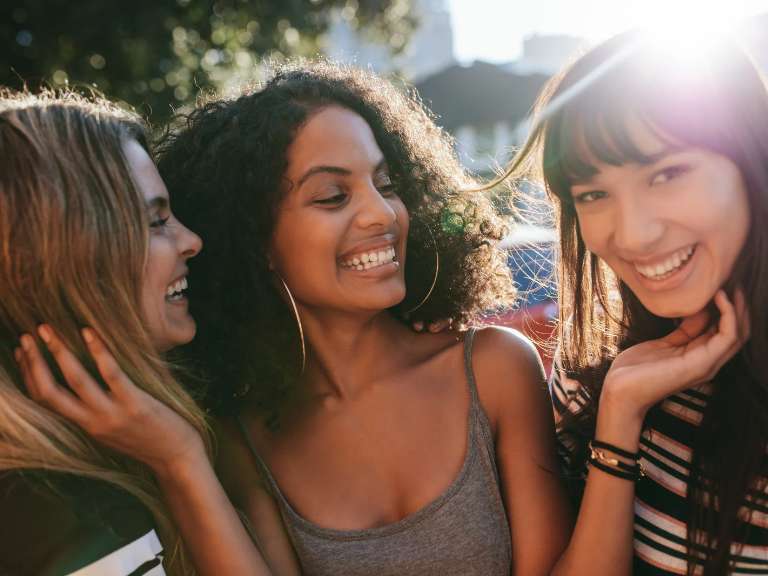 Drei junge Frauen stehen nebeneinander und lachen zusammen
