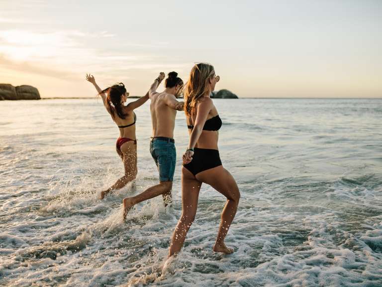 Zwei Frauen und ein Mann sind am Meer und laufen glücklich ins Wasser