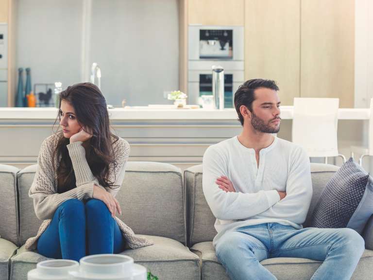 Verzweifeltes Paar sitzt getrennt auf einem Sofa und schaut jeweils in eine andere Richtung