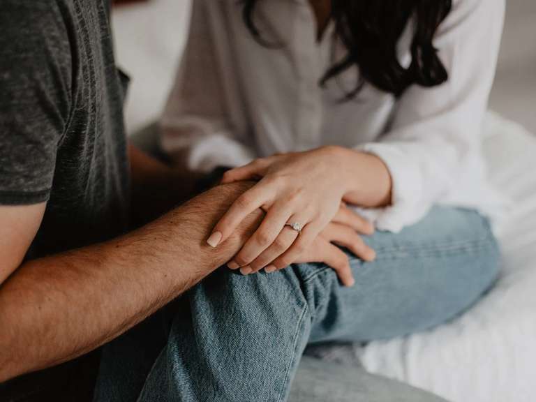 Frau und Mann sitzen auf dem Bett und halten sich gegenseitig die Hände