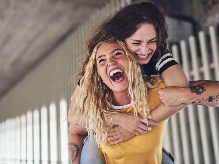 Zwei beste Freundinnen haben Spaß und lachen gemeinsam, ein Mädchen trägt das andere Mädchen auf dem Rücken