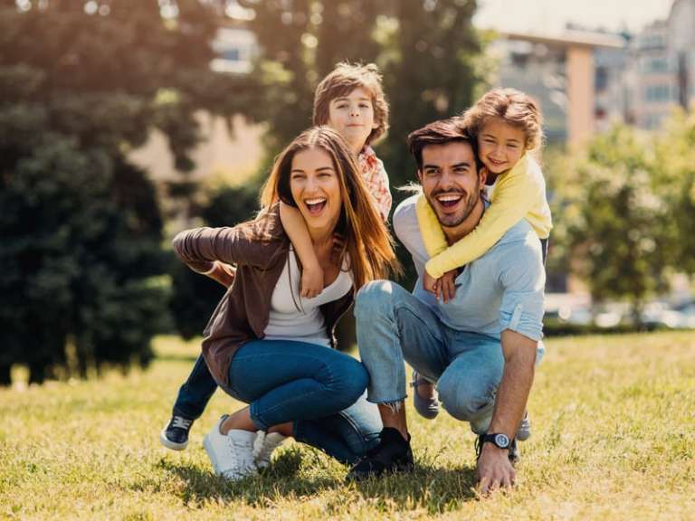 Junge Familie mit einem Sohn und einer Tochter sitzen auf einer Wiese bei Sonnenschein und lachen gemeinsam