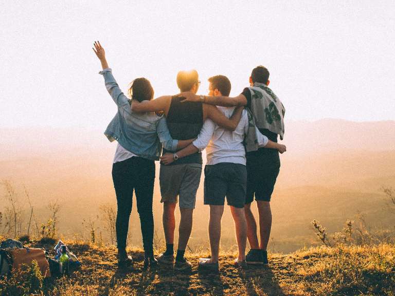 Eine Freundesgruppe mit drei Jungen und einem Mädchen steht auf einem Berg bei Sonnenschein