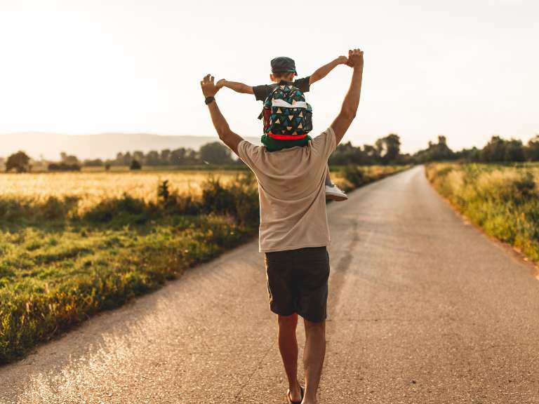 Vater trägt seinen Sohn auf seinen Schultern, während sie bei Sonnenschein spazieren sind