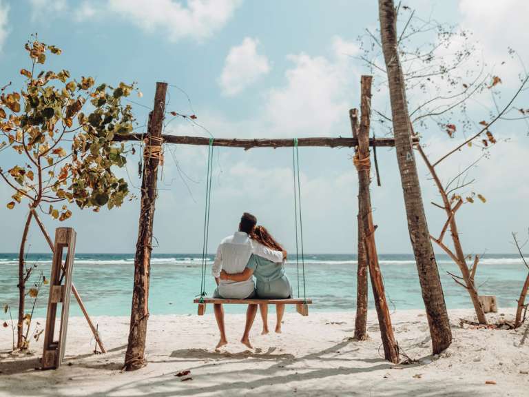 Paar ist auf Flitterwochen und sitzt Arm in Arm auf einer Schaukel am Meer