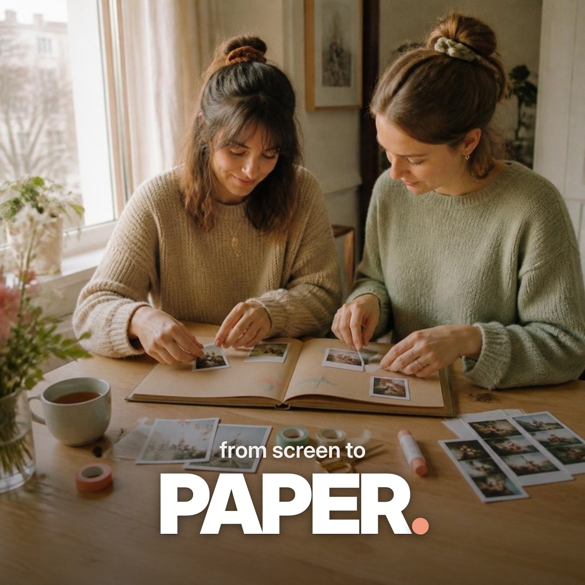 Schriftzug ‚from screen to PAPER.‘ über einem Foto zweier Freundinnen, die an einem hellen Holztisch im Tageslicht Sofortbilder mit Washi-Tape in ein selbstgemachtes Fotoalbum kleben.