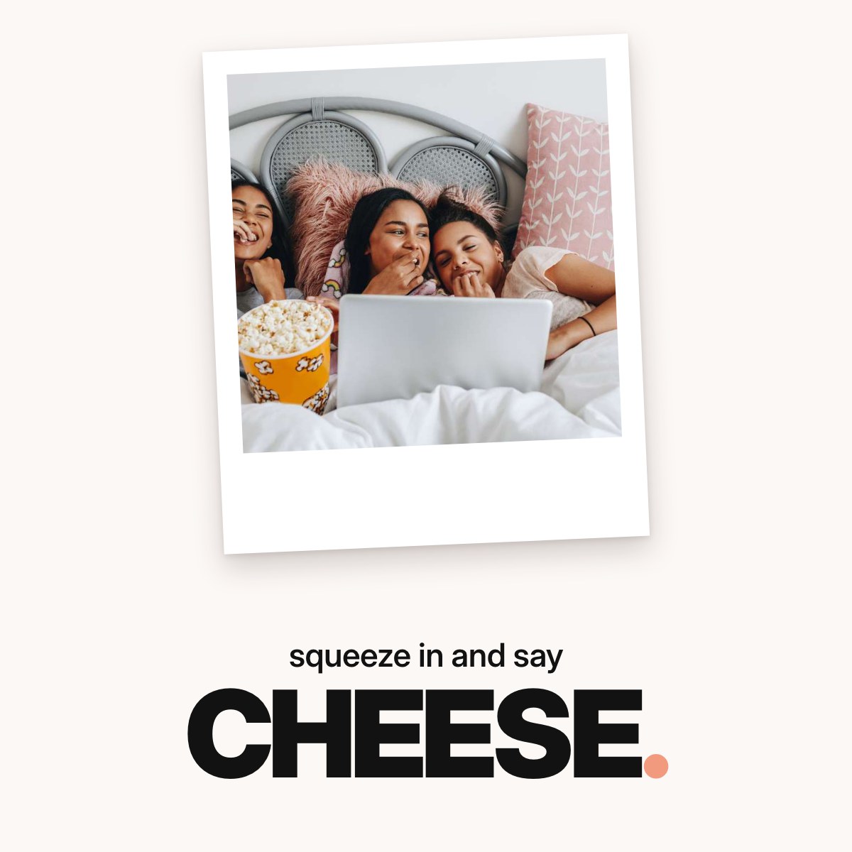 Schriftzug ‚squeeze in and say CHEESE.‘ über einem Foto von drei lachenden Freundinnen, die eng nebeneinander unter einer weißen Decke liegen, Popcorn essen und gemeinsam auf einen Laptop schauen.