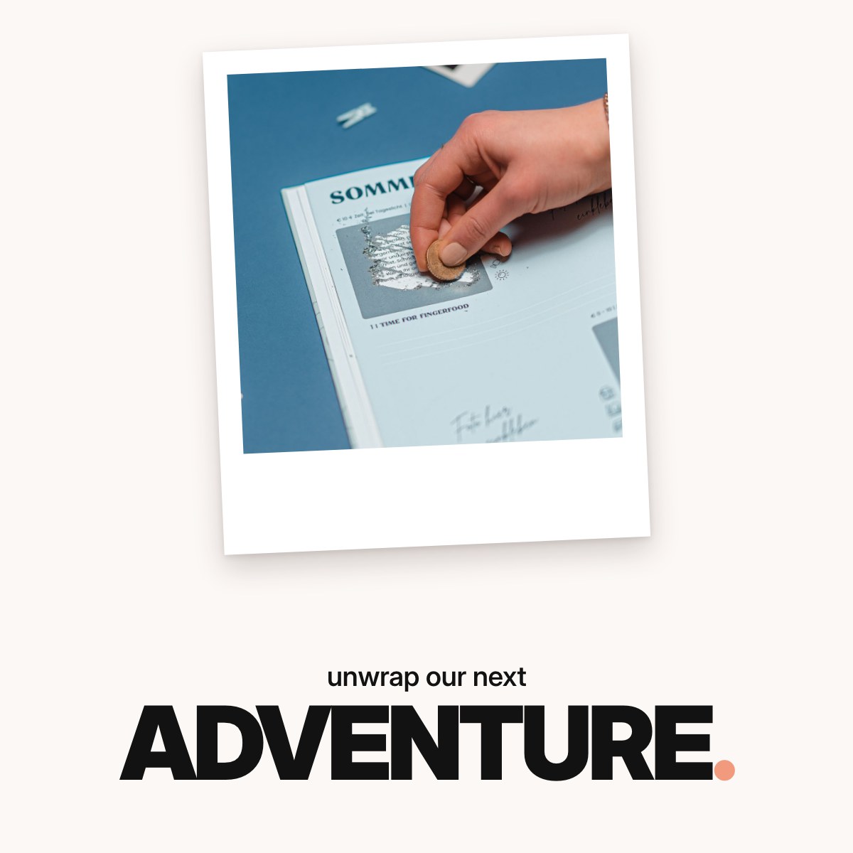 Schriftzug ‚unwrap our next ADVENTURE.‘ über dem mintgrünen Challengebuch für beste Freundinnen in einer Hand, umgeben von Sofortbildfotos, Holzklammern, Washi-Tape und einem Geschenkpaket.