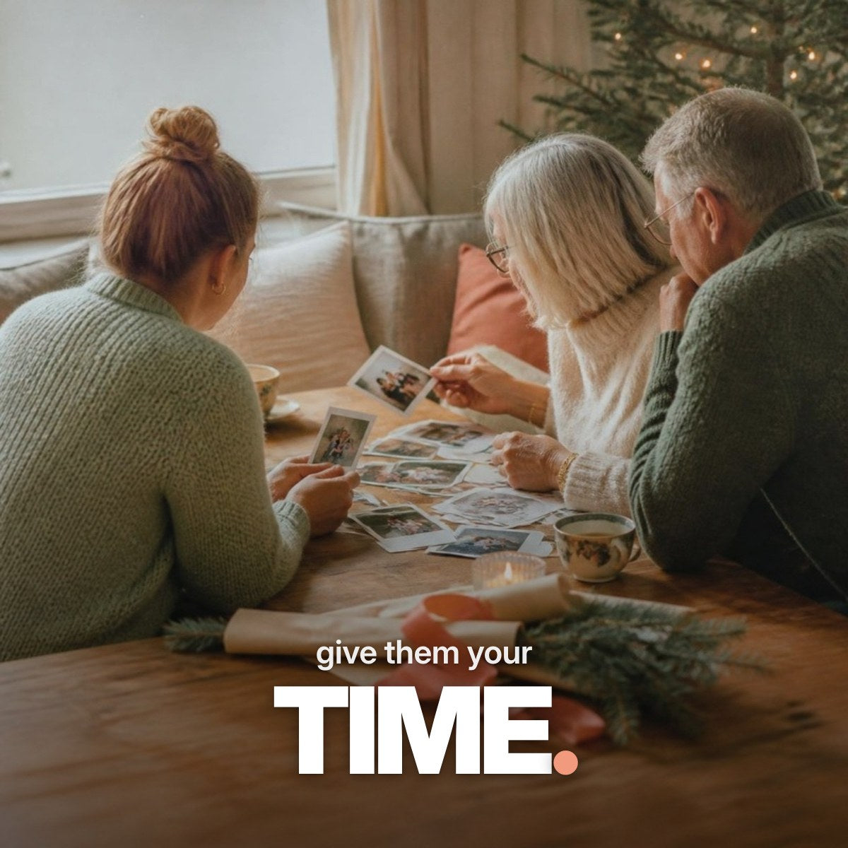 Schriftzug ‚give them your TIME.‘ über einem Foto, auf dem eine erwachsene Tochter mit ihren Eltern an Weihnachten bei Tee und Kerzenlicht alte Familienfotos betrachtet.