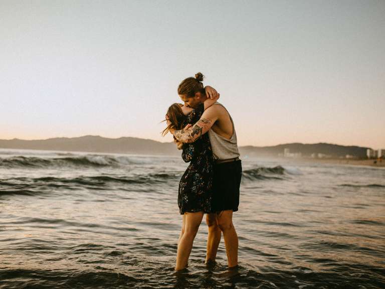 Junges Paar steht im Wasser am Meer und umarmt und küsst sich
