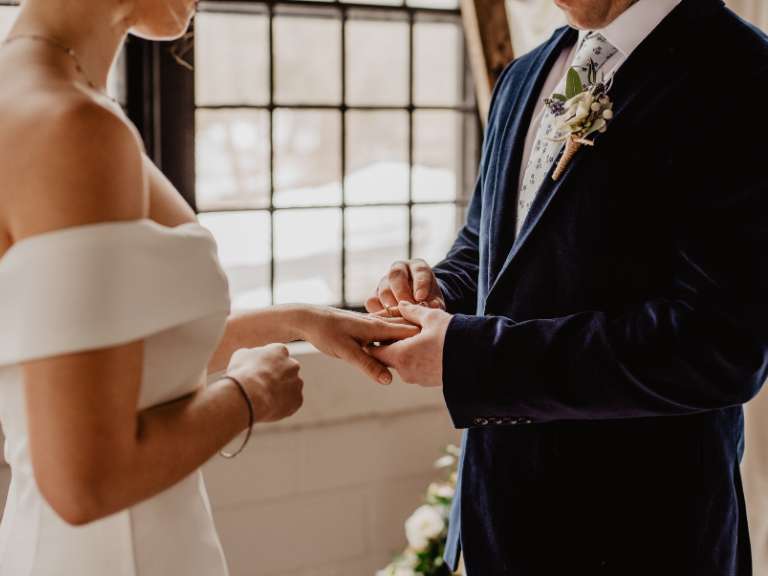 Bräutigam hält die Hand der Braut und steckt ihr den Ehering an