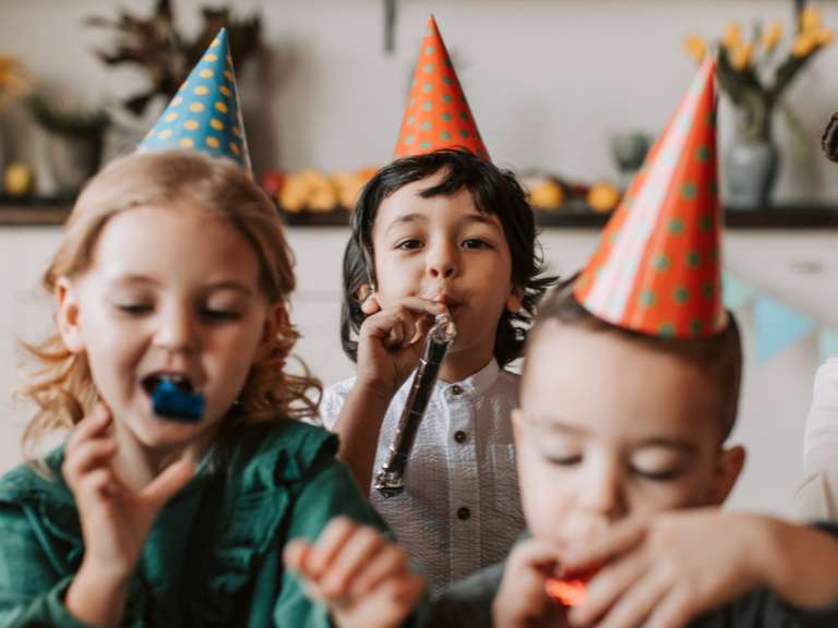 Drei Kinder haben Partyhüte auf und sind auf einem Kindergeburtstag