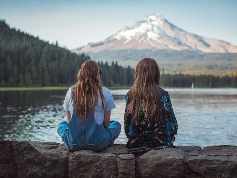 Beste Freundinnen sitzen am Ufer eines Sees und schauen auf das Wasser