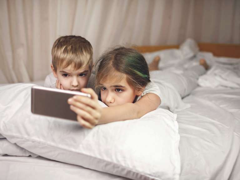Ein kleiner Junge und ein kleines Mädchen Ligen nebeneinander im Bett und schauen auf ein Smartphone