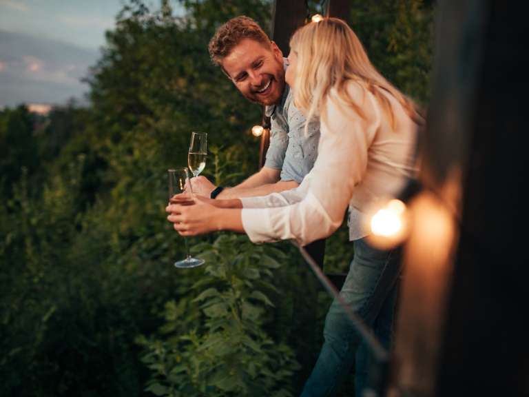 Mann und Frau lehnen sich an einem Geländer an bei romantischer Atmosphäre und lächeln sich gegenseitig an