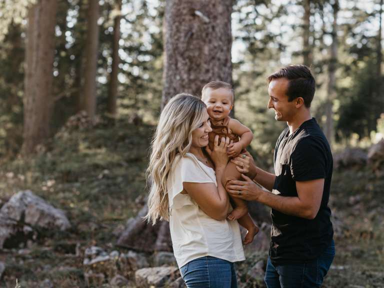 Junge Familie mit einem Kind geht im Wald spazieren, die Mutter hält das Kind auf den Armen