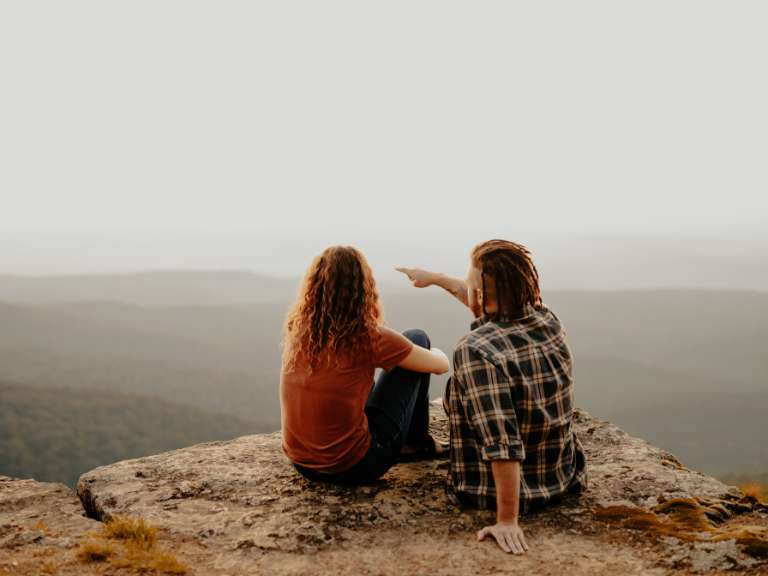 Junges Paar sitzt auf der Spitze eines Berges, beobachtet die Landschaft und genießt den Ausblick