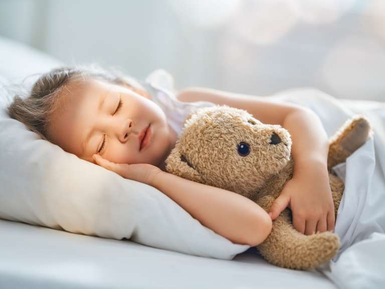 Kleines Mädchen liegt mit ihrem Kuscheltier im Bett und schläft