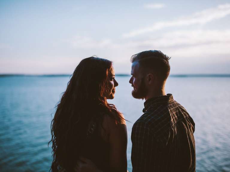Ein Paar steht am Ufer eines Sees und schaut sich in die Augen