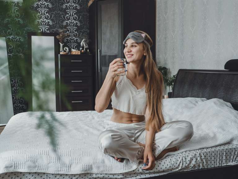Junge Frau im Pyjama sitzt im Bett und hält eine Tasse in der Hand