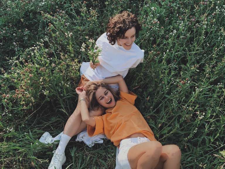 Zwei Freundinnen liegen und sitzen im Gras auf einer grünen Wiese und lachen zusammen