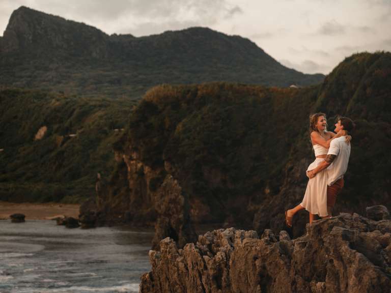 Paar steht auf einem Fels an der Küste und Mann trägt die Frau in seinen Armen