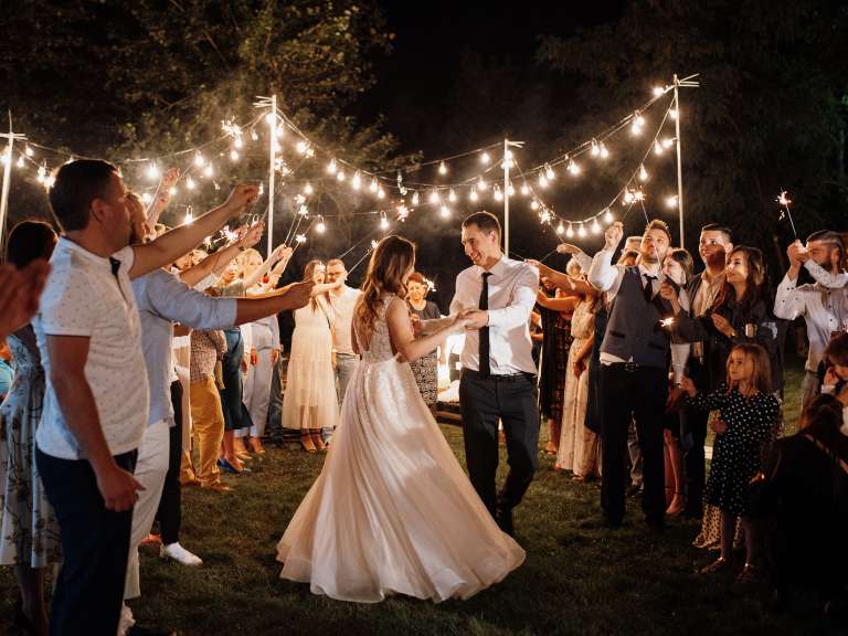 Brautpaar tanzt auf seiner Hochzeit bei romantischer Atmosphäre, währenddessen die Gäste um das Paar herumsteht und ihnen beim Tanz zuschaut