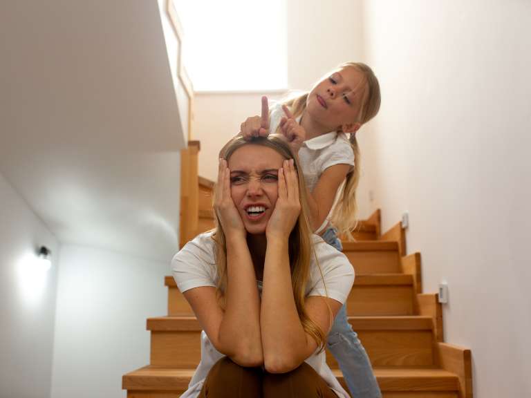 Junge, verzweifelte Mutter sitzt auf der Stufe einer Treppe, ihre Tochter steht hinter ihr und ärgert sie