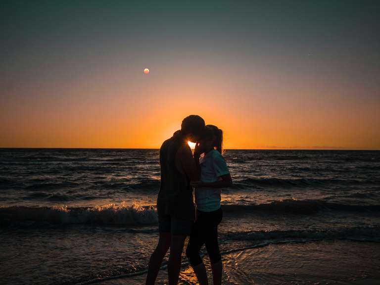 Paar steht am Strand bei Sonnenuntergang und küsst sich
