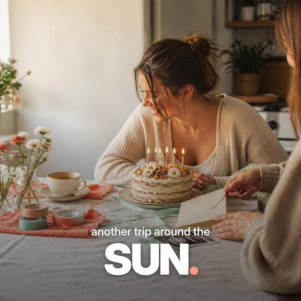 Schriftzug ‚another trip around the SUN.‘ über einem Foto, auf dem eine junge Frau lachend vor einem kleinen Geburtstagskuchen mit Kerzen sitzt, während ihre Freundin ihr eine Karte und Sofortbilder zuschiebt.