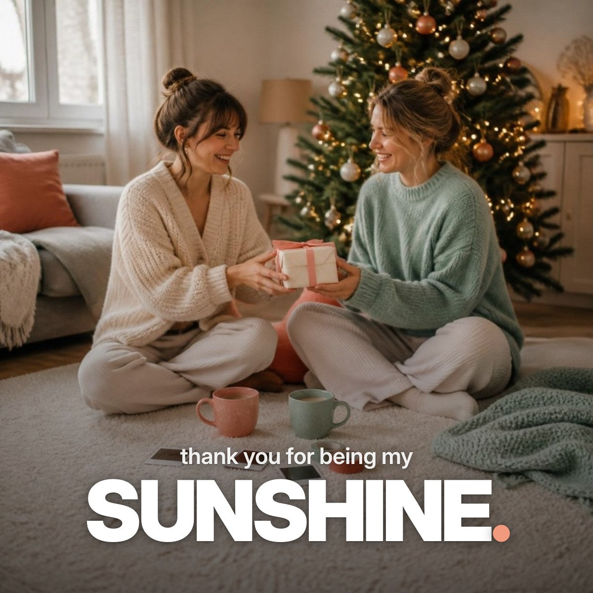 Schriftzug ‚thank you for being my SUNSHINE.‘ über einem Foto zweier lachender Freundinnen, die sich vor einem leuchtenden Weihnachtsbaum auf einem Teppich ein Geschenk mit Korallenschleife überreichen.
